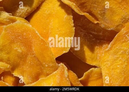 Dried mango slices close-up on a white. Top view. Closeup. Mango chips background. Dehydrated crispy fruit slices, pieces. Heap of sun-dried yellow fr Stock Photo