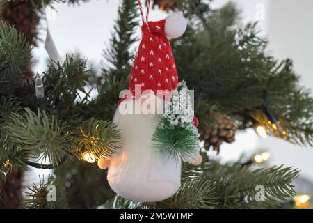 A Christmas tree, Gonk, ornament, hanging from a Christmas Tree holding a miniature Christmas tree with a festive red hat on Stock Photo