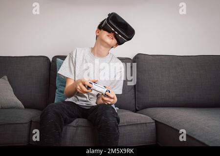 Caucasian boy enjoying at home, gaming using VR box, virtual reality goggles, and simulator, moving and physically interacting with a virtual world Stock Photo