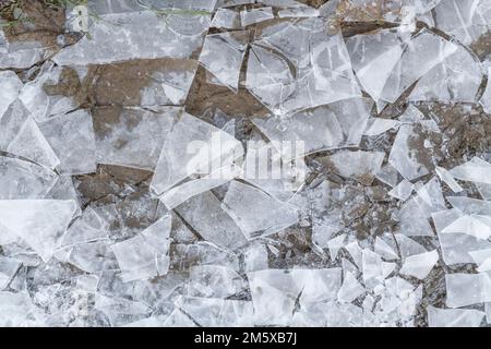 Close shot of shattered broken ice of a frozen puddle on a rural country footpath during UK inter time. For something shattered, or broken promises. Stock Photo