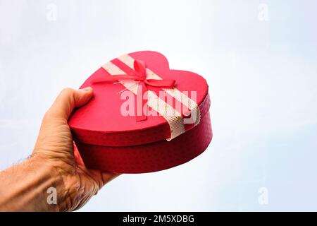 Man's hand giving a gift in a heart-shaped box with a bow, on a white background. Stock Photo