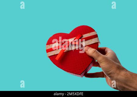 Man's hand giving a gift in the shape of a heart on a blue background. Valentine's Day. Stock Photo