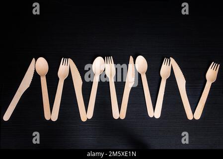 disposable eco-friendly wooden spoons, forks and knives on a dark background Stock Photo