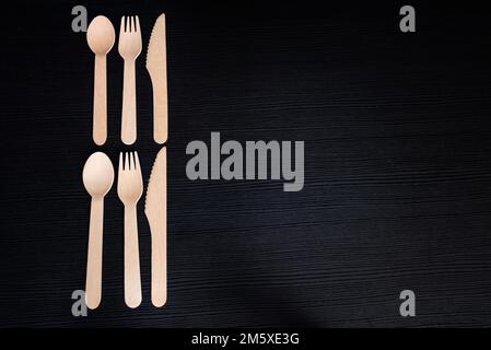 disposable eco-friendly wooden spoons, forks and knives on a dark background Stock Photo