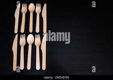 disposable eco-friendly wooden spoons, forks and knives on a dark background Stock Photo