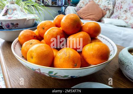 A bowl of clementine fruit in a fruit bowl on a coffee table Stock Photo
