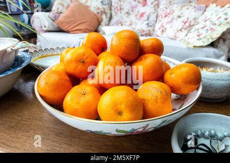 A bowl of clementine fruit in a fruit bowl on a coffee table Stock Photo