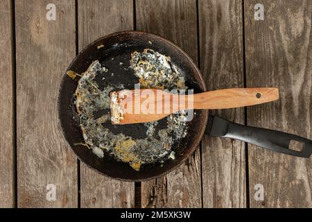 frying pan with food leftovers on a wooden table after breakfast in the kitchen at home Stock Photo