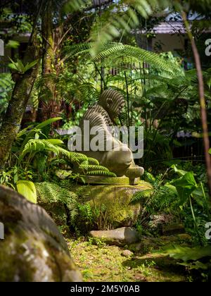 One small stone buddha statue with lush tropical vegetation surrounding it, Berastagi, Indonesia. Taken on a sunny day with no people. Stock Photo