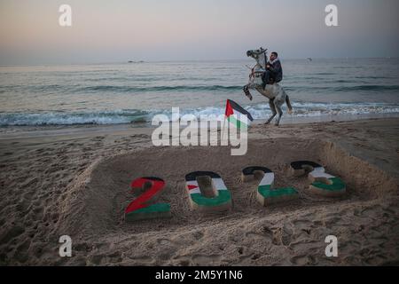 Gaza, Palestine. 31st Dec, 2022. A Palestinian man rides his horse near a sand drawing showing 2023 on the beach of Gaza city during the last sunset of 2022 in Gaza city. (Credit Image: © Ahmed Zakot/SOPA Images via ZUMA Press Wire) Credit: ZUMA Press, Inc./Alamy Live News Stock Photo