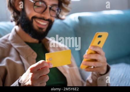 Happy Caucasian man buying things online, using smartphone and credit card, shopping in internet Stock Photo
