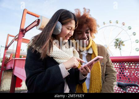 Mixed race young couple in winter clothes with cell phones outdoor. Excited students using mobile Stock Photo