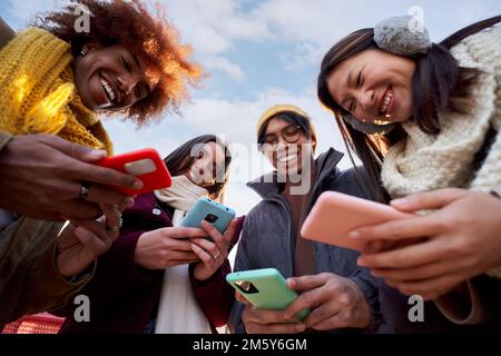 Low angle view of a smiling group of young people using mobile phone. Technology connection addicted Stock Photo