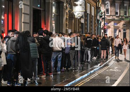 Wardwick, Derby, December 31st 2022. - Huge queues formed at nightclubs with some revellers failing to get inside before midnight in Derby. The club moomoo had the largest queue that streched around the block. Revellers used coats to shelter from the rain whilst they walked between clubs from Wardwick to Friar Gate in Derby city centre just minutes from midnight. Thousands of partygoers packed the bars and clubs as celebrations continued into the new year. Credit: Ben Formby/Alamy Live News Stock Photo