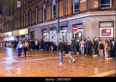 Wardwick, Derby, December 31st 2022. - Huge queues formed at nightclubs with some revellers failing to get inside before midnight in Derby. The club moomoo had the largest queue that streched around the block. Revellers used coats to shelter from the rain whilst they walked between clubs from Wardwick to Friar Gate in Derby city centre just minutes from midnight. Thousands of partygoers packed the bars and clubs as celebrations continued into the new year. Credit: Ben Formby/Alamy Live News Stock Photo