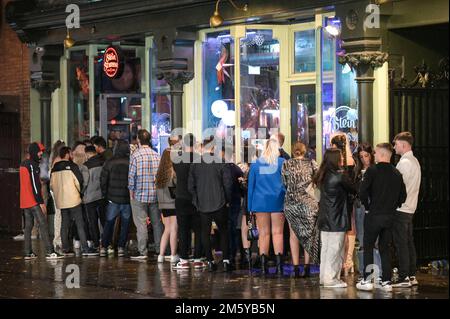 Wardwick, Derby, December 31st 2022. - Huge queues formed at nightclubs with some revellers failing to get inside before midnight in Derby. The club moomoo had the largest queue that streched around the block. Revellers used coats to shelter from the rain whilst they walked between clubs from Wardwick to Friar Gate in Derby city centre just minutes from midnight. Thousands of partygoers packed the bars and clubs as celebrations continued into the new year. Credit: Ben Formby/Alamy Live News Stock Photo