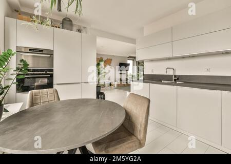 a kitchen and dining area in a modern home with white cabinets, marble countertops, stainless appliances and a round table Stock Photo