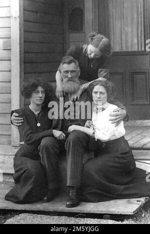 A father is surrounded by his daughters and wife sitting on his porch stoop, ca. 1905. Stock Photo