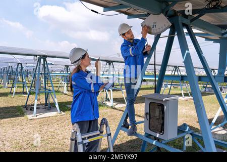 Maintenance engineer at solar farm stand on structure support checking solar panel angle indicator Stock Photo