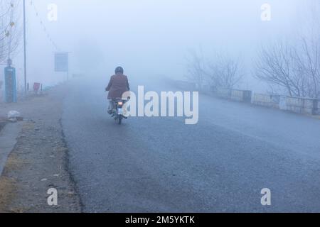 Man riding on a bike going for work in thick fog in swat valley, Pakistan