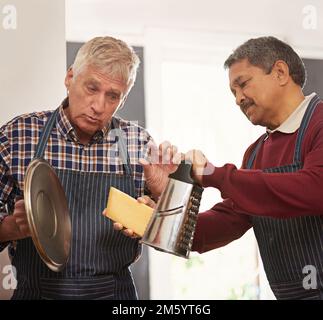 Dont be scared to add a little more cheese. two senior men cooking in the kitchen. Stock Photo