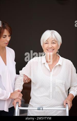 My daughter takes good care of me. a woman assisting her elderly mother whos using a walker for support. Stock Photo