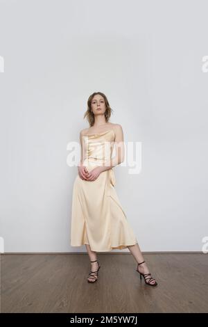 Female model wearing beige camisole silk top and wrapped midi skirt. Stylish and elegant monochrome summer outfit. Fashion Studio shot. Stock Photo