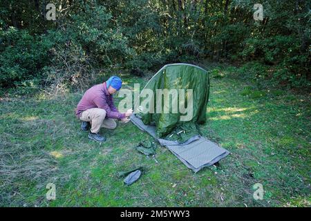 man setting up a tent in a forest glade of Sicily in Etna Park, Italy Stock Photo