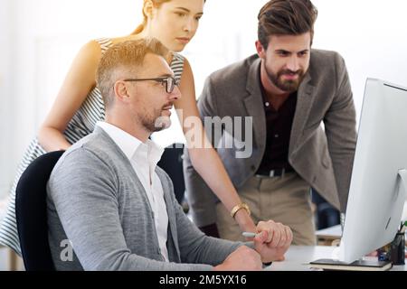 Making great progress on their project. a group of designers working together at a computer. Stock Photo