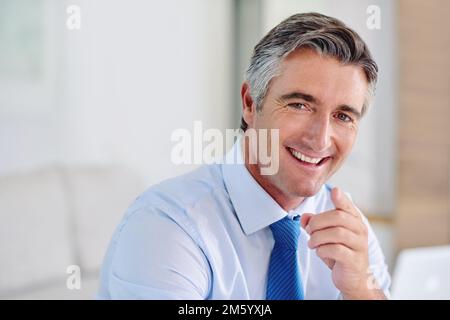 Watch out world. Portrait of a confident mature businessman wearing a suit and sitting indoors while pointing at the camera. Stock Photo