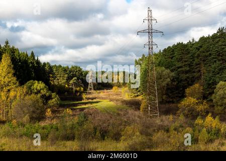 High-voltage power line passing through a picturesque valley surrounded by autumn nature, electric wires suspended on high metal poles Stock Photo