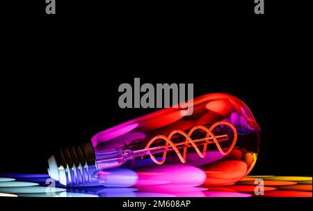 Colourful patterns reflect within a clear glass, oval shaped lightbulb and photographed against a black background Stock Photo