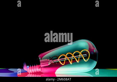 Colourful patterns reflect within a clear glass, oval shaped lightbulb and photographed against a black background Stock Photo