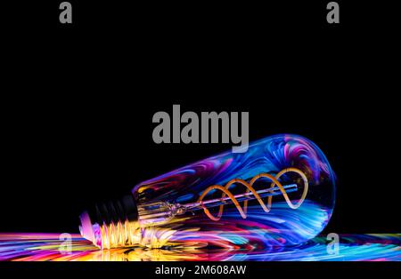 Colourful patterns reflect within a clear glass, oval shaped lightbulb and photographed against a black background Stock Photo