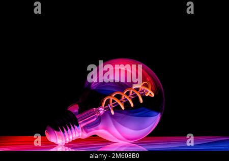 Colourful patterns reflect within a clear glass round shaped lightbulb, photographed against a black background Stock Photo