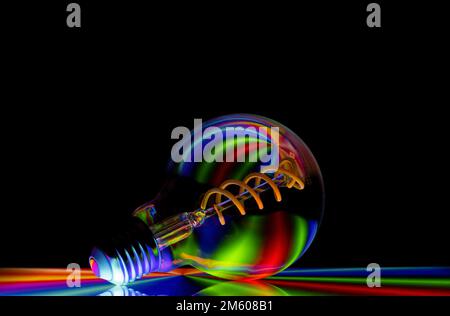 Colourful patterns reflect within a clear glass round shaped lightbulb, photographed against a black background Stock Photo