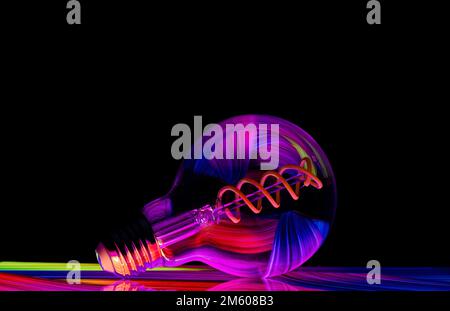 Colourful patterns reflect within a clear glass round shaped lightbulb, photographed against a black background Stock Photo