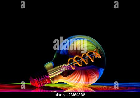 Colourful patterns reflect within a clear glass round shaped lightbulb, photographed against a black background Stock Photo