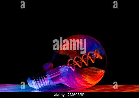 Colourful patterns reflect within a clear glass round shaped lightbulb, photographed against a black background Stock Photo