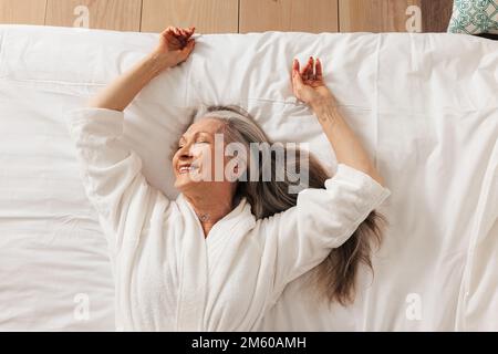 Smiling senior woman lying on bed with closed eyes enjoying morning Stock Photo
