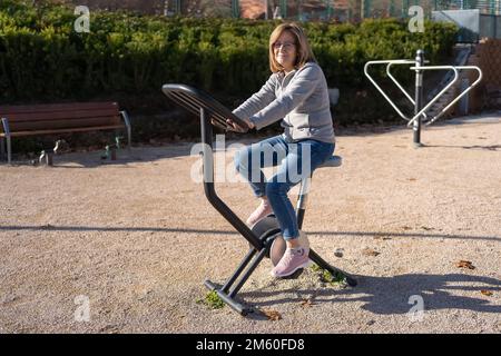 Senior woman riding a stationary bike in a public city park to keep fit. Stock Photo