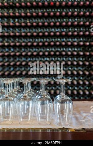 Empty wine glasses with many stacked bottles as a background, preparation to wine tasting in the winery of Lanzarote, Spain Stock Photo