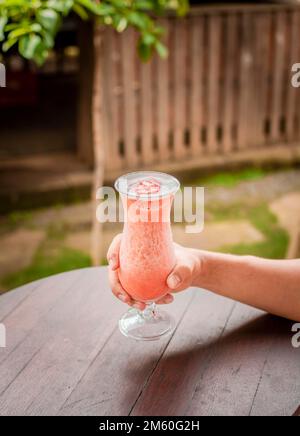 Top view of hand holding a strawberry milkshake on table, Hands showing strawberry smoothie on wooden table. Hands holding strawberry smoothie on Stock Photo