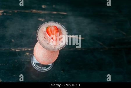 View of strawberry milkshake on dark wood. View from above of delicious strawberry smoothie with a strawberry on top on wood. Top view of strawberry Stock Photo