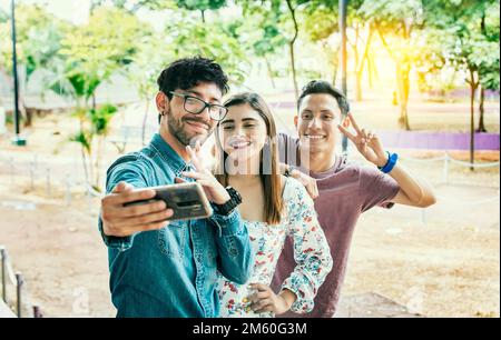 Happy friends taking a selfie in a park. Three friends standing taking a selfie in the park. Portrait of three smiling friends taking a selfie on the Stock Photo