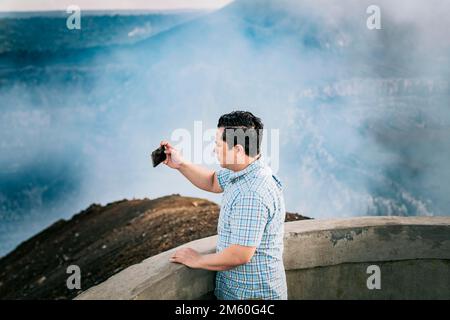 Tourist man taking photos at a viewpoint. Young tourist man taking photos at a volcanic viewpoint. Adventurous man with his cell phone taking photos Stock Photo
