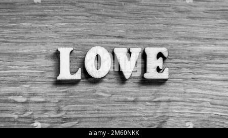 Love - word inscription of 3D wooden letters on the wood textured board background. Expression of romantic theme or Valentines Day. Rustic style inscription. Black and white image. Stock Photo