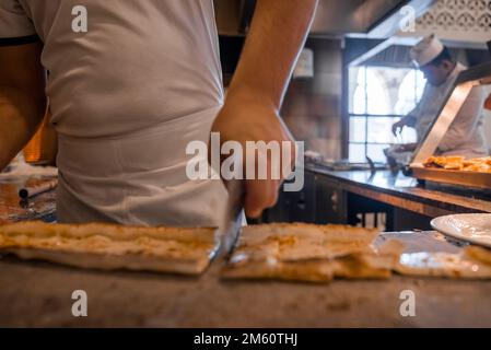 Chef cutting Turkish pide into slices on table at restaurant