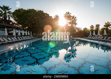 Deck chairs and parasols arranged around swimming pool at resort Stock Photo