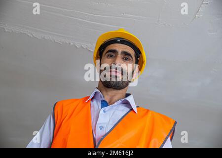 A plasterer in construction wears overalls and a hat. He is plastering a wall with finishing putty using a putty knife. Repair work and construction c Stock Photo